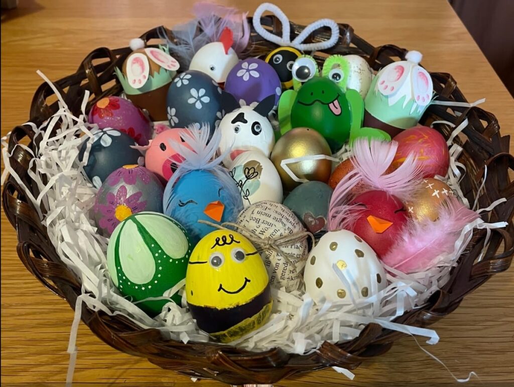A wicker bowl holding brightly painted eggs, including some that look like frogs, bluebirds, pandas & flowers.